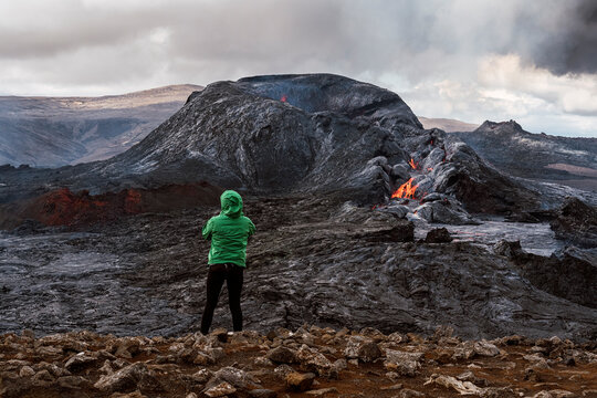 Anonymous tourist admiring erupting volcano under cloudy sky