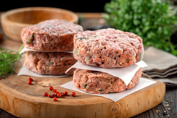 Frozen spicy pork patties with seasonings on table. Butcher minced meat cutlet, close up