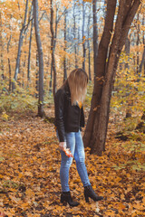 Lonely sad woman is kicking yellow leaves in autumn. Sad mood and seasonal affective disorder concept.