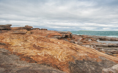 Fototapeta na wymiar Big boulders of red rock and sea waves against the dramatic sky background