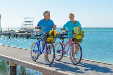 Older couple, seniors, riding bicycles on the beach in tropical blue outfits at sunset, romantic, fitness