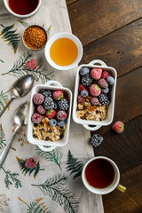 Oatmeal in square ceramic bowls with frozen berries. Porridge with raspberries, blackberries, blueberries and strawberries in white plates on a wooden table with a tablecloth.