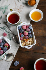 Oatmeal in square ceramic bowls with frozen berries. Porridge with raspberries, blackberries, blueberries and strawberries in white plates on a wooden table with a tablecloth.