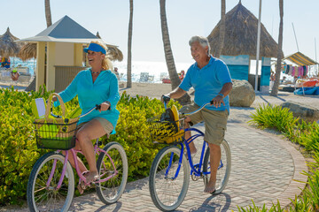 Older couple, seniors, riding bicycles on the beach in tropical blue outfits at sunset, romantic, fitness