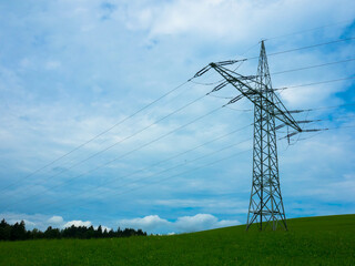 High-voltage power lines that run through a green meadow, on a background of a cloudy sky.
