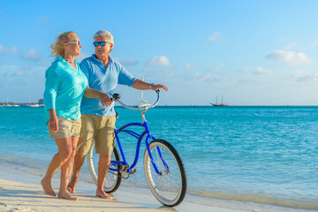 Obraz na płótnie Canvas Older couple, seniors, riding bicycles on the beach in tropical blue outfits at sunset, romantic, fitness