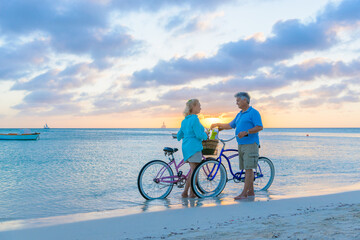 Older couple, seniors, riding bicycles on the beach in tropical blue outfits at sunset, romantic, fitness