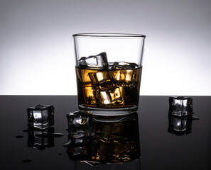 Whiskey on the rocks in a transparent glass on a mirrored black table