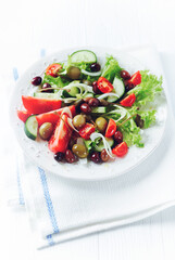 Healthy salad with various tomatoes, cucumber, olives and capers. White wooden background. 