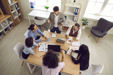 Fototapeta Team of businesspeople having a discussion in a meeting. Group of young and mature business teammates sitting around table in office interior and listening to manager. View from above, high angle shot obraz