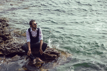 man with a beard in dark clothes and a white shirt lie on the stone seashore in Crimea tarkhankut