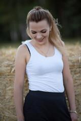 Fototapeta premium Portrait of a young beautiful blonde girl in a light dress on the field near the straw.