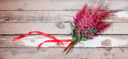 Bouquet of beautiful red and pink astilbe flowers with red ribbon on aged wooden background