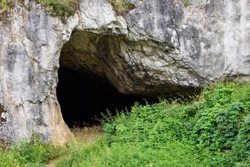 The entrance to the cave in the rock with grass in the foreground.