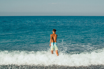 teen boy walking on the beach at waves