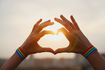 Gay pride, love and marriage concept. Hands with gay pride LGBT rainbow flag wristband making heart...