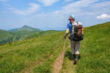 A sports tourist with a large backpack walks along a mountain trail in the Ukrainian carpathians overlooking Hoverla, the highest mountain in Ukraine