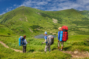 Three tourists with large backpacks stand on a trail in the Ukrainian Carpathians and look at Lake...