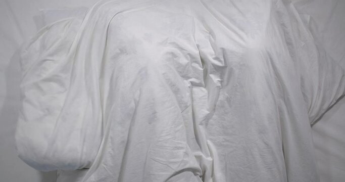  Top view of caucasian couple having sex to bed   in light room. High angle shooting.  Man amd woman making love under a blanket. They look at each other, smile and hide under a blanket 4k 