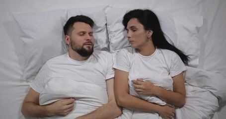  Top view of caucasian couple sleeping in bed with white linens in light room. High angle shooting. Man snoring loudly and woman cant sleep 4k 