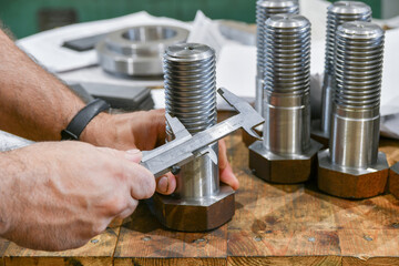 The worker measures the diameter of the thread on the bolt with a vernier caliper, after turning....