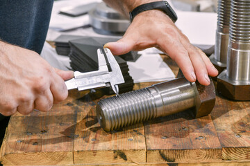 The worker measures the thread pitch on the bolt with a vernier caliper, after turning. Quality control department.