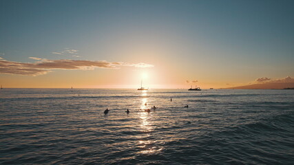 Amazing colors of a tropical sunset. Silhouettes of sailing boats floating on the ocean horizon. Surfers ride the waves. Oahu, summer vacation in Hawaii. Slow motion.