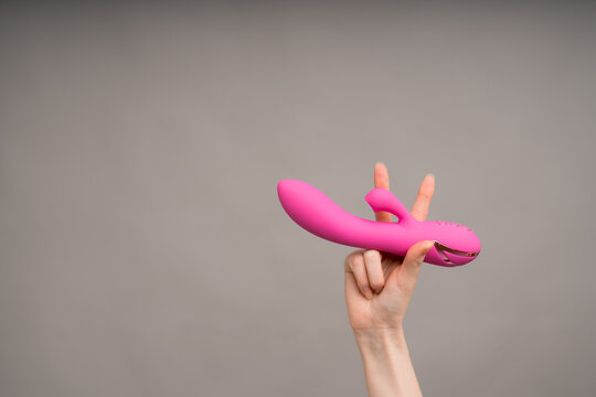 A woman's hand holds a pink dildo or massager for sex and shows the Victoria gesture with her fingers.