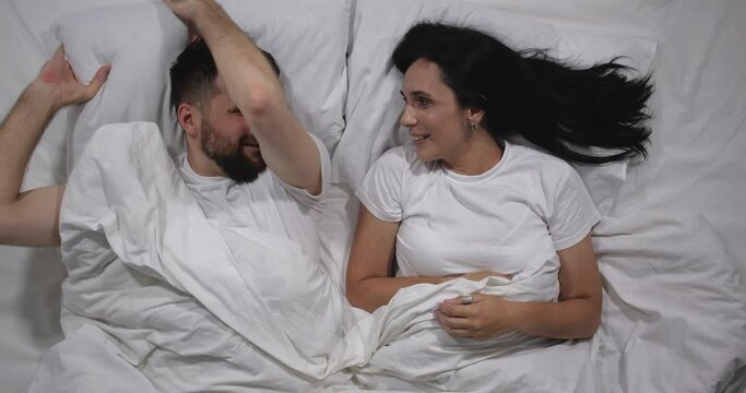  Top view of caucasian couple kidding in bed   in light room. High angle shooting.  Man amd woman fighting with pillows 4k 