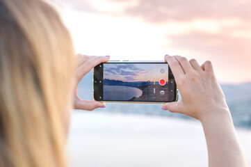 Girl using cell phone for taking sea landscape photo, south sunset
