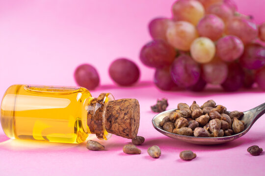 Grape seed oil in a glass jar and fresh grapes on a pink background.