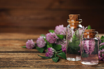 Obraz na płótnie Canvas Beautiful clover flowers and bottles of essential oil on wooden table, closeup. Space for text