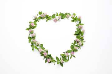 Heart shaped frame of beautiful clover flowers with green leaves on white background, top view. Space for text