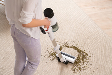 Young woman uses cordless vacuum cleaner to clean home carpet. Close-up of mung bean brush from...