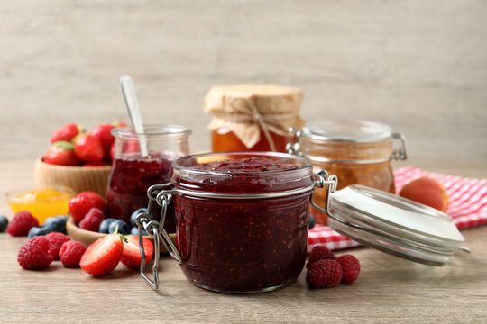 Jars with different jams and fresh fruits on wooden table