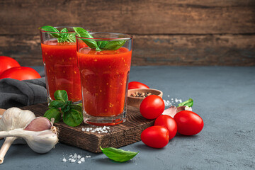 Two glasses of tomato juice with basil and spices on a wooden background. Side view, space for copying.