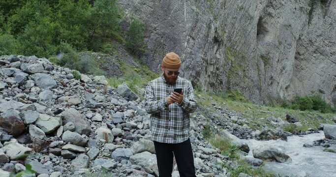 The Caucasus. Young man takes pictures on phone standing near a mountain river