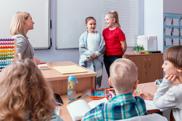 Two girls are standing together in front of a class full of children