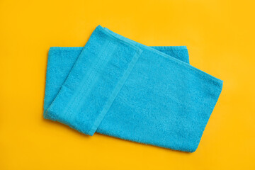 Folded light blue beach towel on yellow background, top view