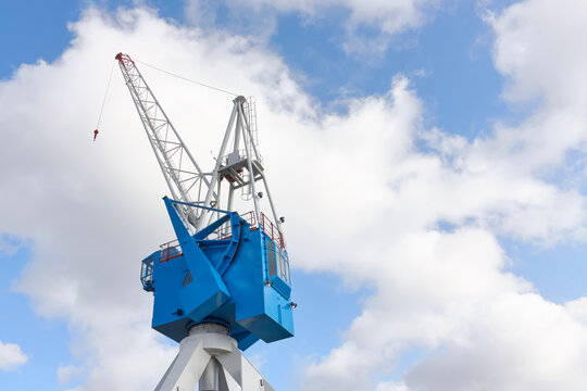 Blue and grey painted steel dock crane against a blue sky with clouds.