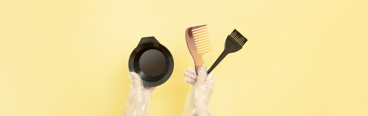 Brushes and bowl for home or salon hair dyeing in the hands of a woman with gloves on yellow background