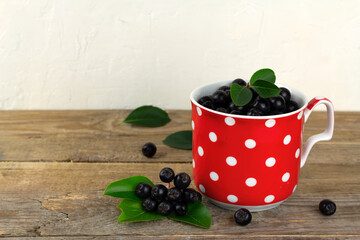 Fresh chokeberry in a red cup on wooden background
