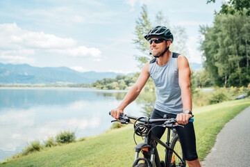 Portrait of a sincerely smiling man dressed in cycling clothes, helmet and sunglasses riding a...