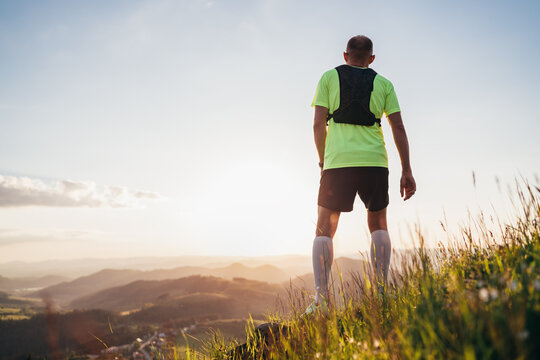 Backview of Active mountain trail runner dressed bright t-shirt with backpack enjoying the sunset while he sky running by picturesque hills at sunset time. Sporty active people concept image