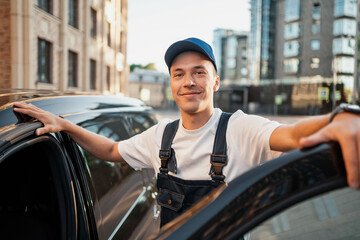 A satisfied good male courier works in a courier service in a uniform by car.