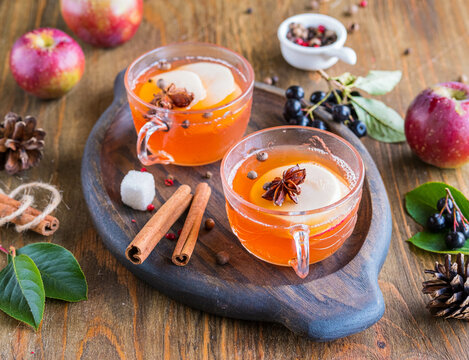 Autumn hot drink, spicy apple cider with apple slices in cups on a wooden tray. American cuisine.
