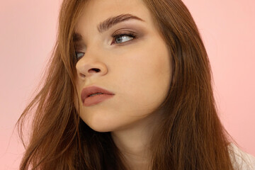 Fototapeta premium Beautiful teenage girl with long hair and blue eyes on pink background.Girls Face looking sexy to the Camera. Fashionable Makeup, very long Lashes.