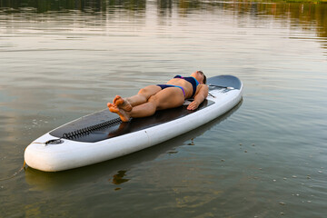 A lonely woman lies on Sup Bord surrounded by a lake at sunset. Lake Lebyazhye, Kazan. Active...