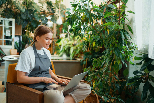 A female florist works in the garden. Agronomist surf the Internet looking for information about flowers. Home plants for sale.