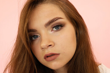 Naklejka premium Beautiful teenage girl with long hair and blue eyes on pink background.Girls Face looking sexy to the Camera. Fashionable Makeup, very long Lashes.
